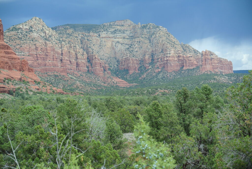 A vast landscape showcasing red rock formations and green forest under a cloudy sky, possibly taken closer to Sedona.
