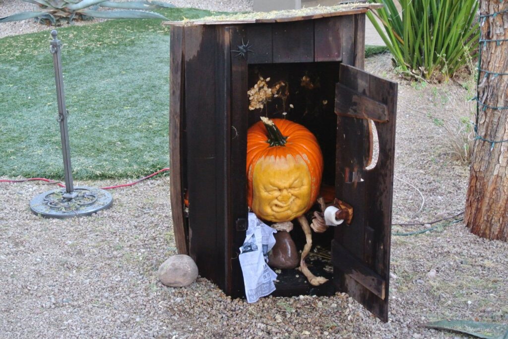 A large pumpkin sculpture with a menacing face is inside a small wooden shed in the garden. Perfect for Halloween, this angry pumpkin clutches a rope, adding an eerie touch to the fall decor.