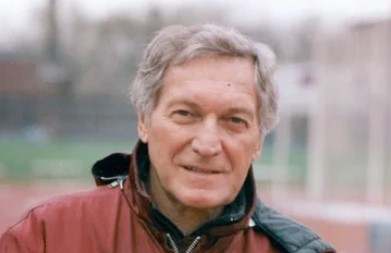 An older man with gray hair, reminiscent of a local legend, is wearing a red jacket and standing outdoors.