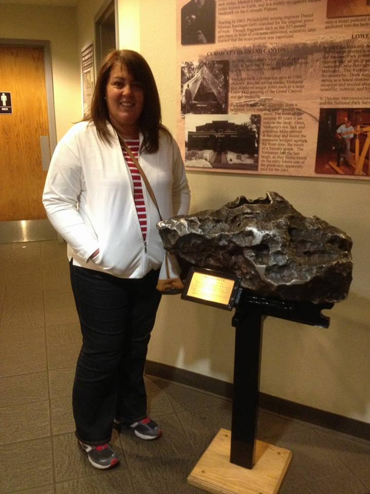 A woman stands next to a large rock displayed on a stand in a museum hallway, with informational plaques on the wall behind her.