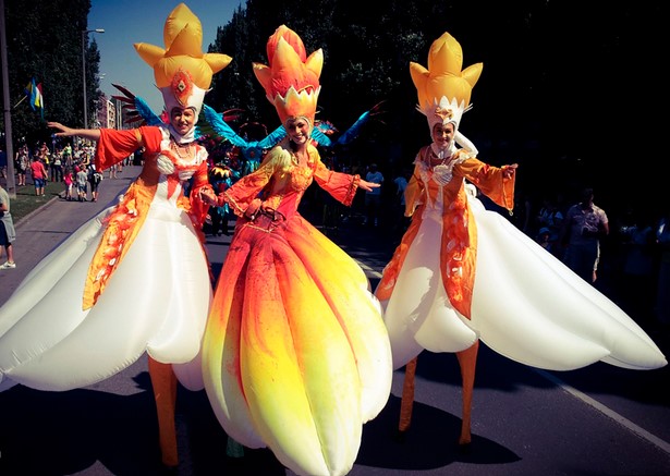 In Alcoy, three people wearing colorful, flower-themed costumes perform on stilts during a parade that started with vibrant music and lively cheers.
