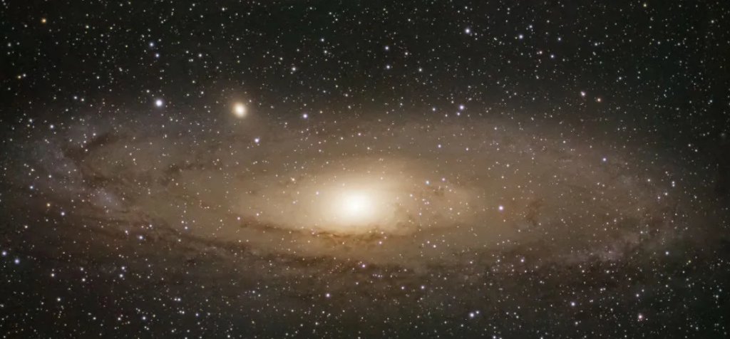 The image shows a spiral galaxy with a bright core surrounded by a disk of stars and dust, set against a backdrop of numerous smaller stars in space.