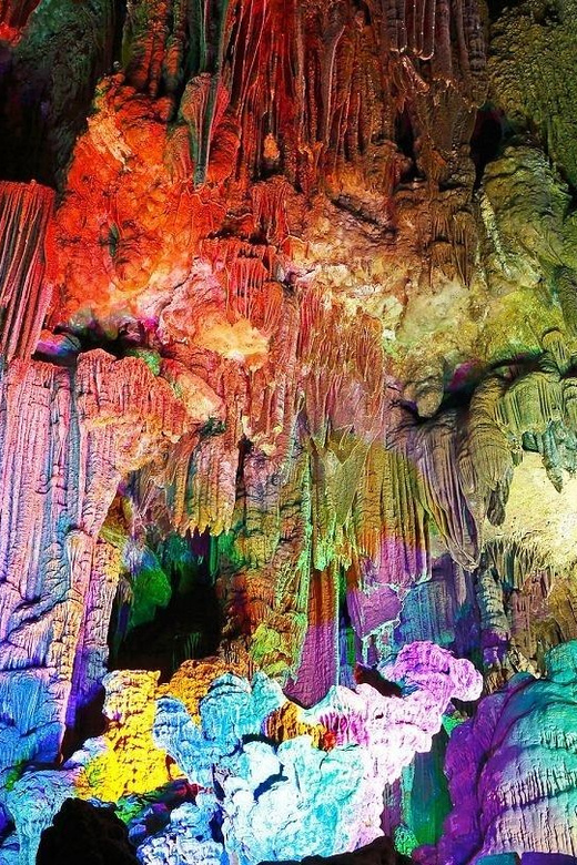 Exploring the colorfully lit cave interior, where stalactites and stalagmites create a spectrum of light from red to blue, reveals hidden wonders that form a vibrant and surreal atmosphere.
