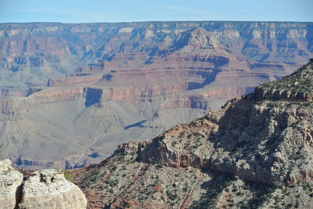 Layered rock formations and steep cliffs of the Grand Canyon under a clear blue sky invite SUV travel, showcasing geological features and rugged terrain perfect for adventure seekers.