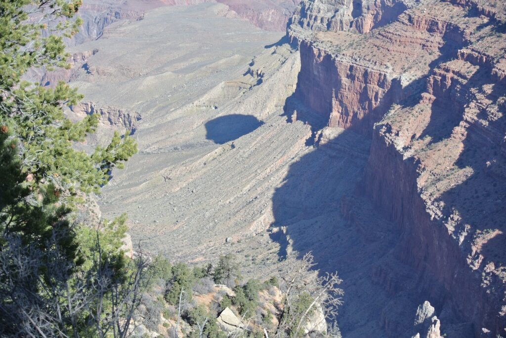 View of a rocky canyon landscape with steep cliffs and sparse vegetation, perfect for travel enthusiasts exploring by SUV. Dramatic shadows stretch across the terrain, reminiscent of the majestic Grand Canyon.